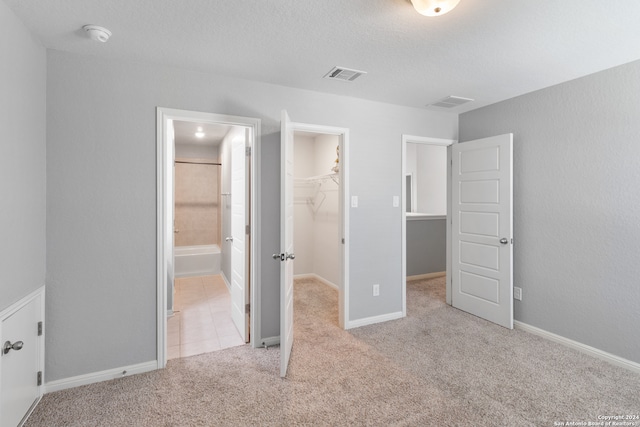 unfurnished bedroom featuring a textured ceiling, light colored carpet, a spacious closet, and a closet