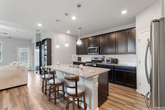 kitchen with a center island with sink, pendant lighting, stainless steel appliances, and light hardwood / wood-style floors