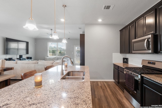 kitchen with light stone countertops, pendant lighting, dark wood-type flooring, stainless steel appliances, and sink