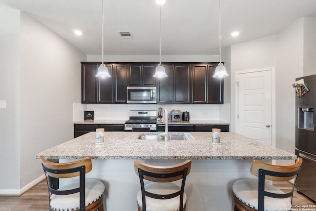 kitchen featuring a kitchen island with sink, appliances with stainless steel finishes, hardwood / wood-style flooring, and decorative light fixtures