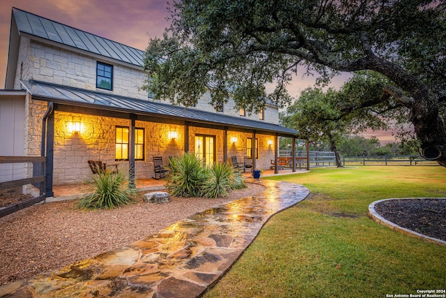 back house at dusk with a lawn and a patio