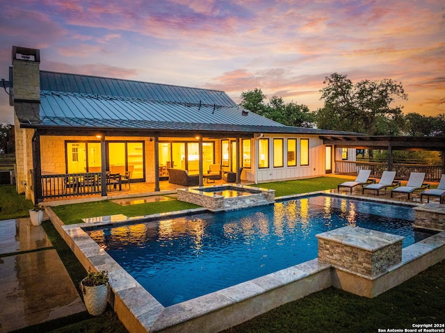 pool at dusk featuring an in ground hot tub, a yard, and a patio