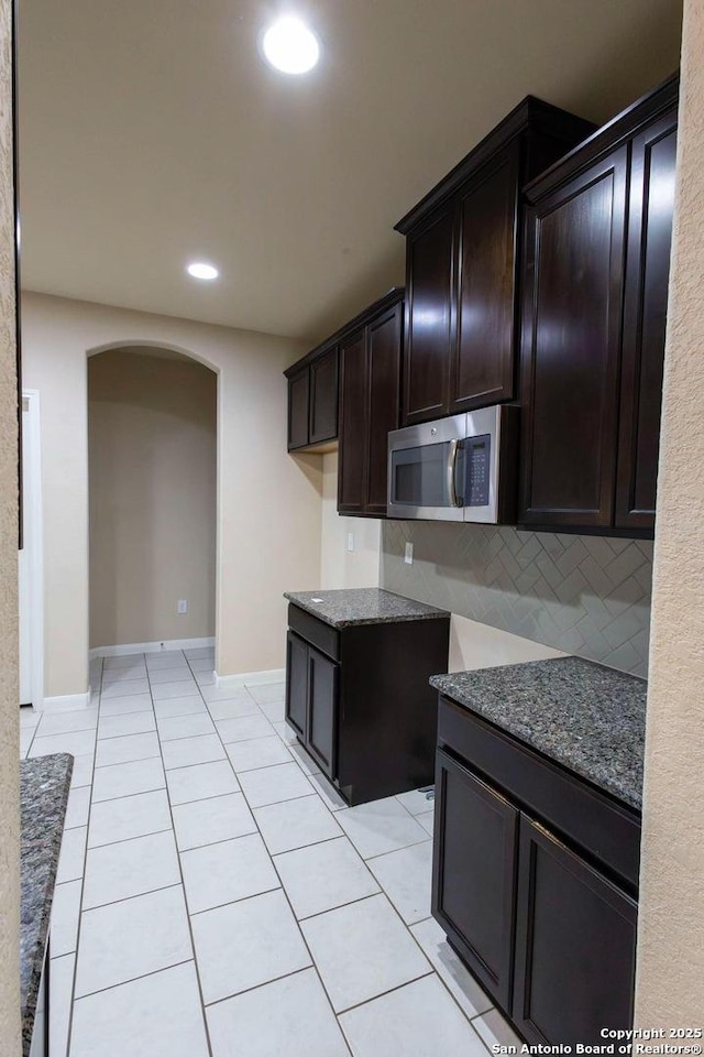 8446 Buckhorn Parke, San Antonio, TX 78254 - kitchen with stone countertops, tasteful backsplash, stainless steel microwave, arched walkways, and dark brown cabinets