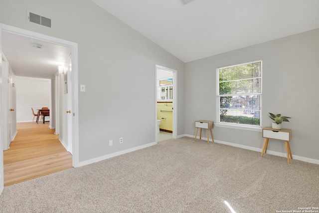 unfurnished bedroom with light carpet, ensuite bath, and vaulted ceiling