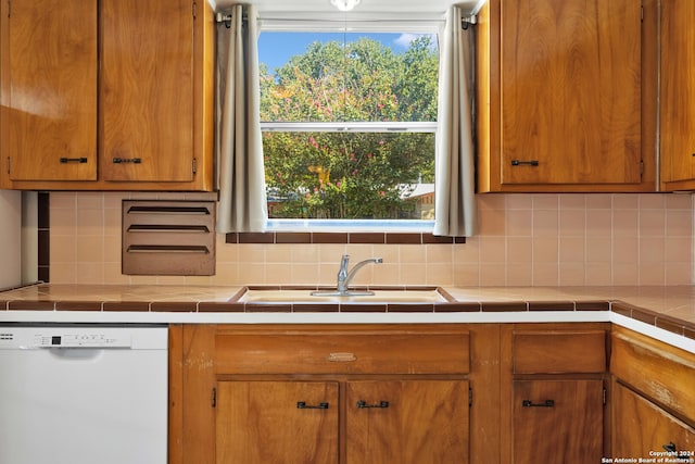 kitchen with tasteful backsplash, tile countertops, sink, and white dishwasher