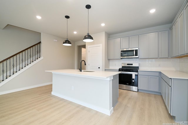 kitchen featuring an island with sink, a sink, stainless steel appliances, and light countertops