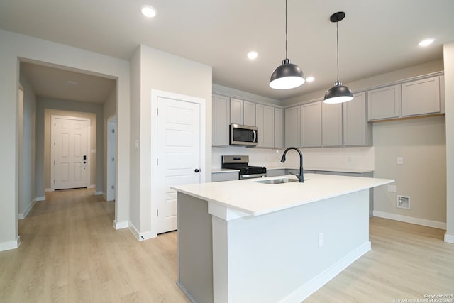 kitchen with a center island with sink, light countertops, light wood-style flooring, appliances with stainless steel finishes, and a sink