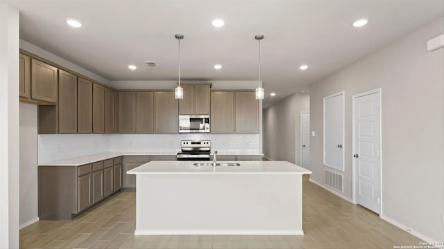 kitchen with decorative light fixtures, sink, a kitchen island with sink, and appliances with stainless steel finishes