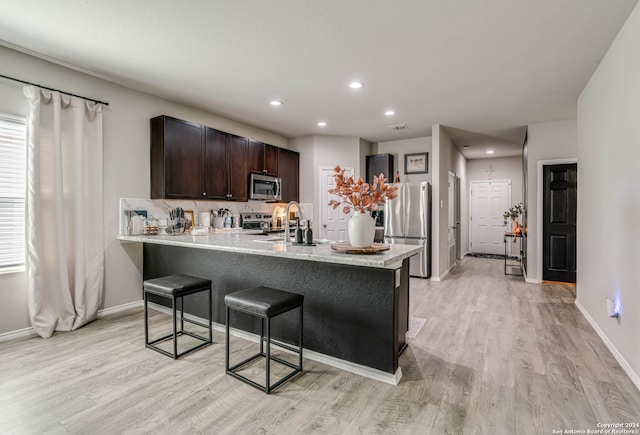 kitchen with appliances with stainless steel finishes, light hardwood / wood-style floors, dark brown cabinets, kitchen peninsula, and a breakfast bar area