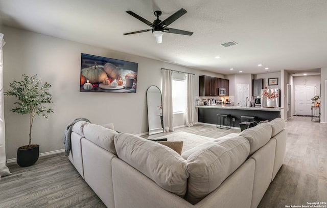 living room with light wood-type flooring, sink, and ceiling fan