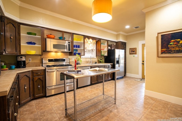 kitchen with light tile patterned flooring, appliances with stainless steel finishes, tile countertops, ornamental molding, and dark brown cabinetry