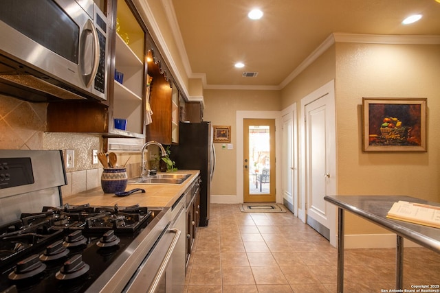 kitchen featuring sink, crown molding, light tile patterned floors, stainless steel appliances, and backsplash