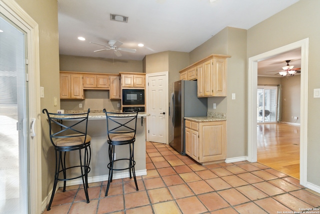 kitchen featuring black appliances, light hardwood / wood-style flooring, light brown cabinetry, a breakfast bar, and ceiling fan