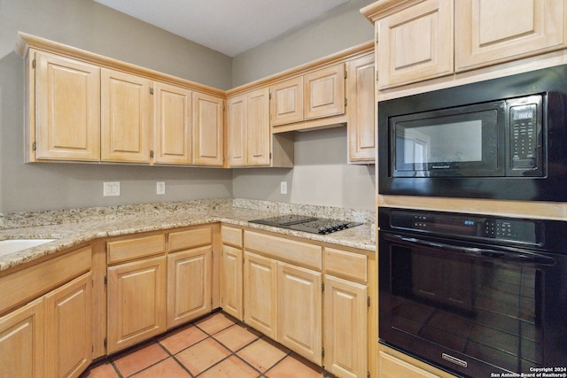 kitchen with black appliances, light brown cabinets, light tile patterned floors, and light stone countertops