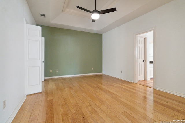 empty room with light wood-type flooring, a tray ceiling, and ceiling fan