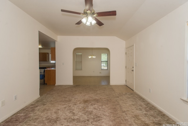 carpeted empty room featuring vaulted ceiling and ceiling fan with notable chandelier