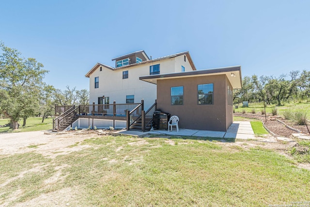 back of property with a yard, a wooden deck, and a patio area