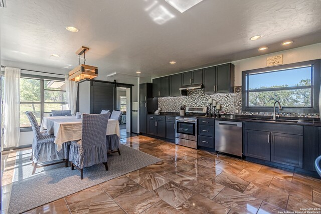 kitchen featuring tasteful backsplash, stainless steel appliances, decorative light fixtures, sink, and a barn door