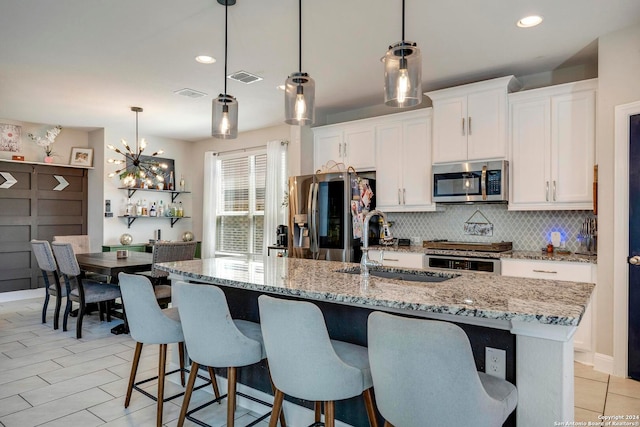 kitchen featuring a kitchen island with sink, stainless steel appliances, light stone countertops, hanging light fixtures, and white cabinets