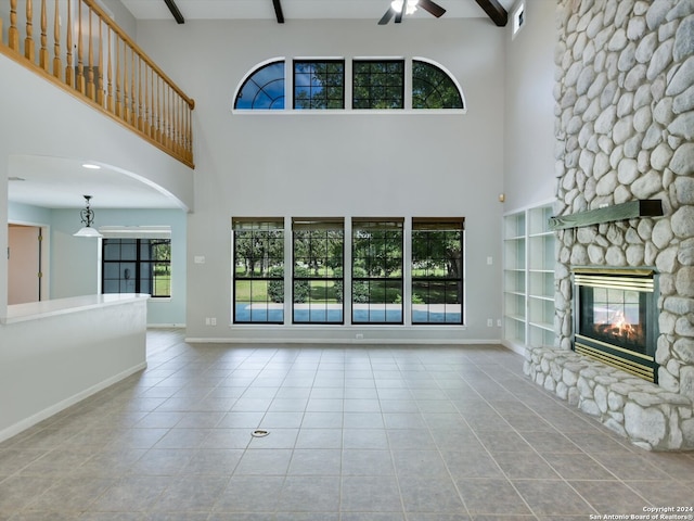 unfurnished living room featuring beamed ceiling, a high ceiling, ceiling fan, and a stone fireplace