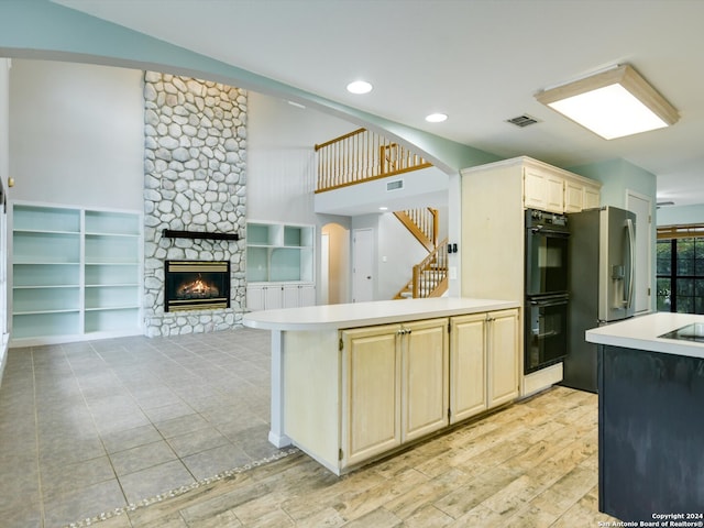 kitchen with black double oven, stainless steel fridge, a fireplace, and kitchen peninsula