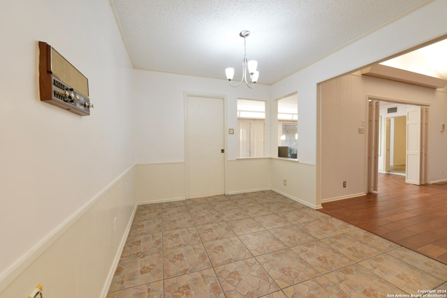 empty room with a textured ceiling, a chandelier, and wood-type flooring