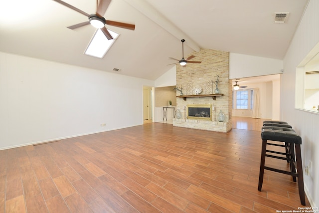 living room featuring wood-type flooring, a skylight, a fireplace, beamed ceiling, and high vaulted ceiling