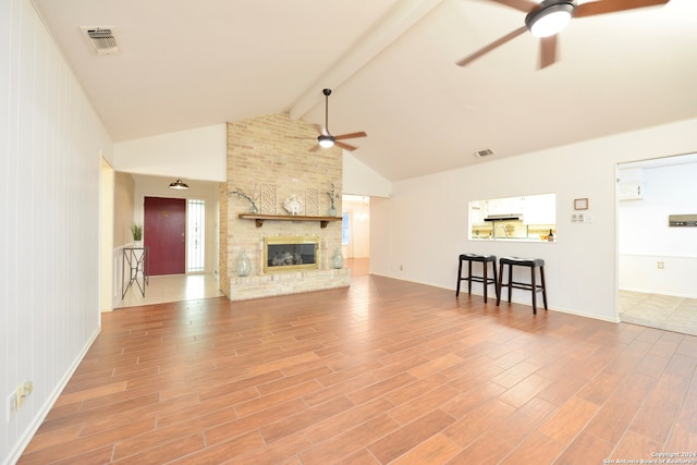 unfurnished living room with a large fireplace, light hardwood / wood-style flooring, lofted ceiling with beams, and ceiling fan