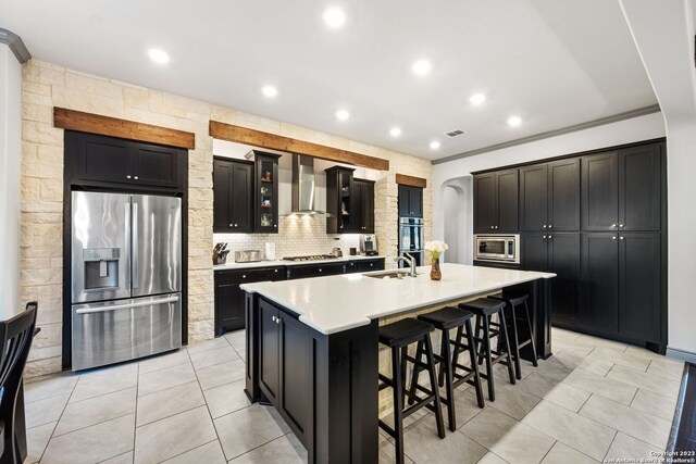 kitchen featuring stainless steel appliances, sink, wall chimney exhaust hood, a center island with sink, and ornamental molding