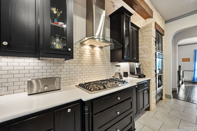 kitchen with crown molding, backsplash, light tile patterned floors, stainless steel appliances, and wall chimney range hood