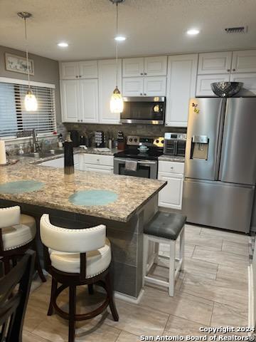 kitchen featuring appliances with stainless steel finishes, pendant lighting, white cabinetry, and a breakfast bar area