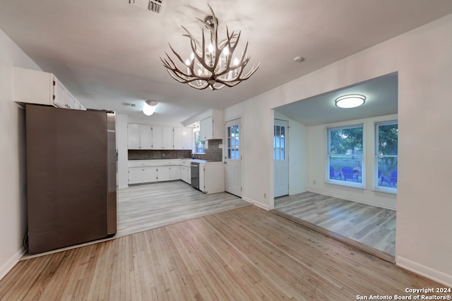 kitchen with white cabinetry, light hardwood / wood-style flooring, backsplash, stainless steel appliances, and hanging light fixtures