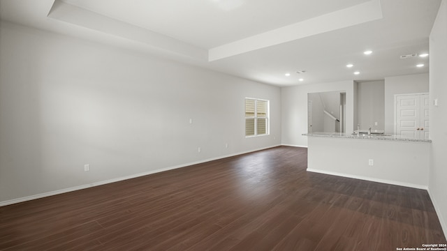 unfurnished living room featuring a raised ceiling, dark hardwood / wood-style flooring, and sink