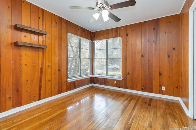 unfurnished room with wood walls, ceiling fan, and wood-type flooring