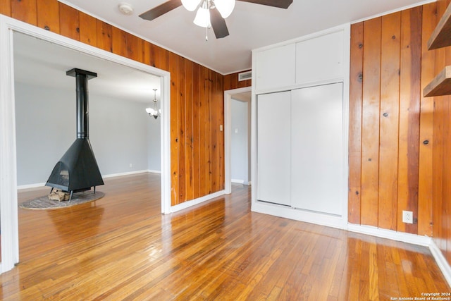 interior space with a wood stove, ceiling fan, wood walls, and hardwood / wood-style floors