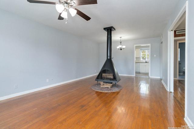 interior space with ceiling fan with notable chandelier, hardwood / wood-style floors, sink, and a wood stove