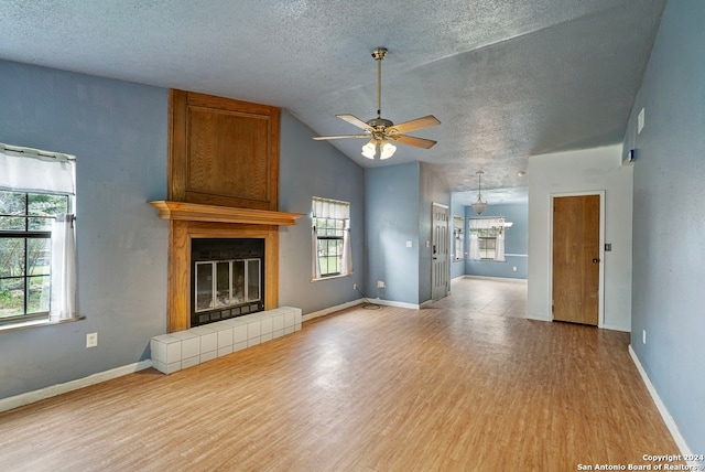 unfurnished living room featuring a tile fireplace, ceiling fan, vaulted ceiling, and light wood-type flooring