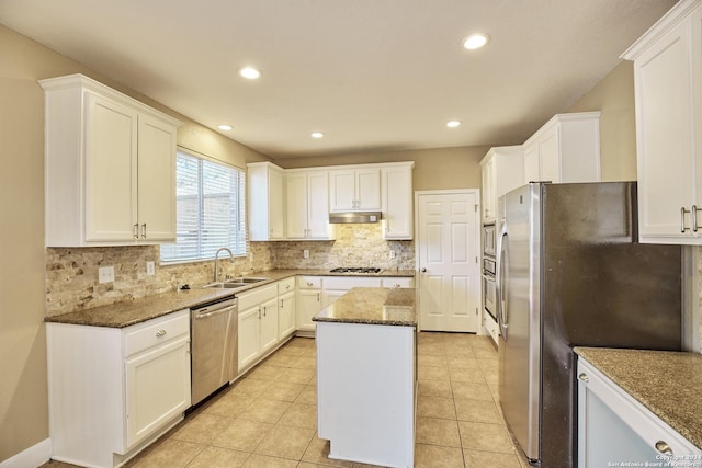 kitchen with under cabinet range hood, stainless steel appliances, a sink, a kitchen island, and decorative backsplash