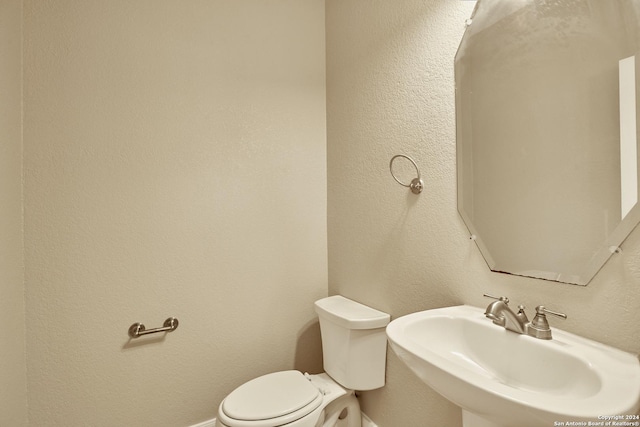 half bath featuring a textured wall, baseboards, a sink, and toilet