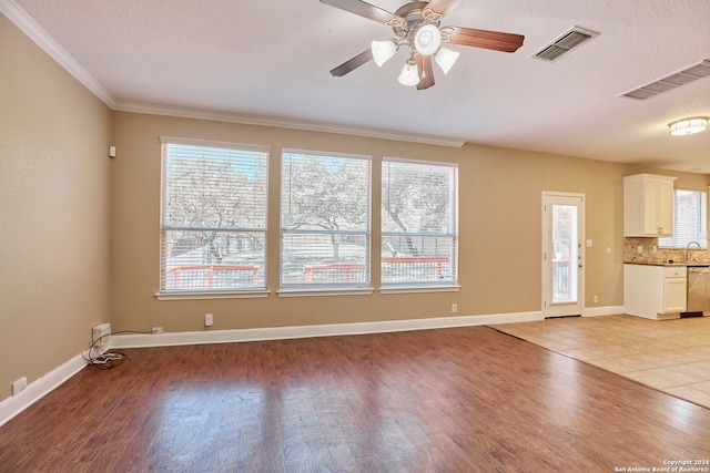 unfurnished living room featuring ceiling fan, plenty of natural light, ornamental molding, and light wood-type flooring