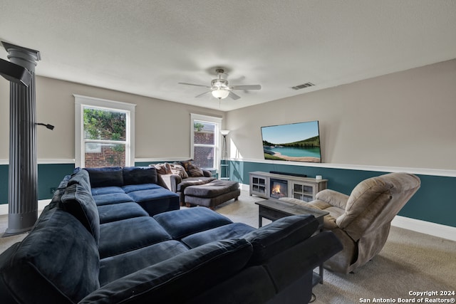 carpeted living room featuring a textured ceiling, ceiling fan, a fireplace, and decorative columns