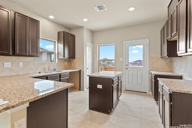 kitchen featuring a kitchen island, light stone counters, light tile patterned floors, and tasteful backsplash