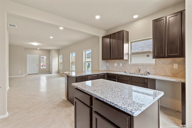 kitchen featuring light stone counters, kitchen peninsula, sink, and decorative backsplash