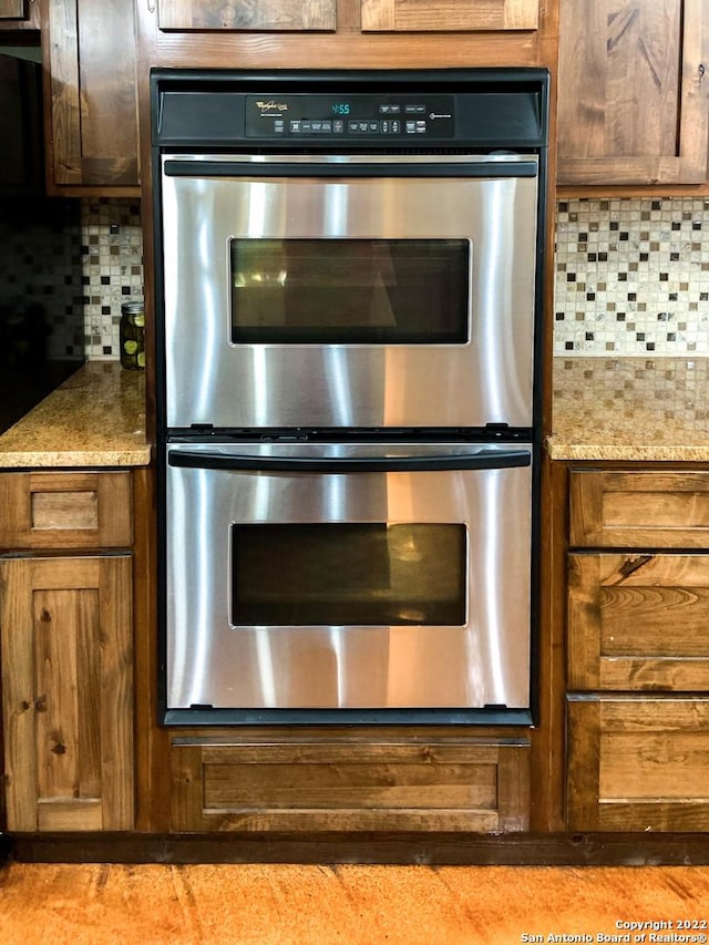 kitchen with brown cabinets, double oven, tasteful backsplash, and light stone countertops