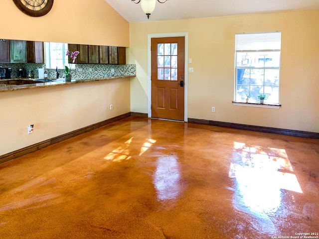 foyer with lofted ceiling, baseboards, and finished concrete floors