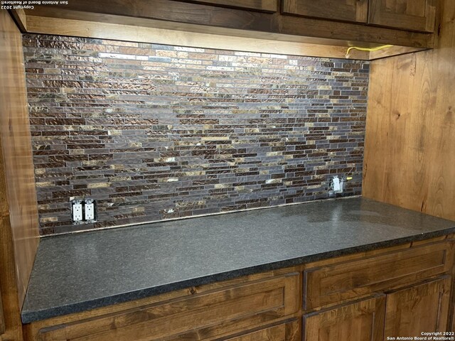 room details with dark countertops, decorative backsplash, and brown cabinetry