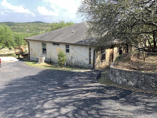 back of property featuring a wooden deck, central AC, a shingled roof, and stone siding