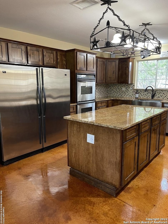 kitchen with a sink, tasteful backsplash, light stone counters, a kitchen island, and appliances with stainless steel finishes