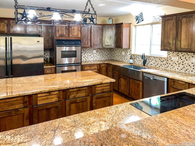 kitchen featuring light stone counters, a sink, decorative backsplash, decorative light fixtures, and appliances with stainless steel finishes