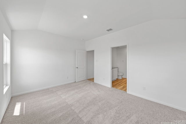 unfurnished bedroom featuring light carpet, vaulted ceiling, and ensuite bathroom